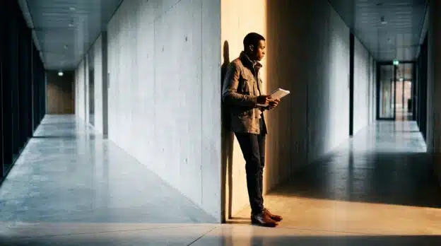 Étudiant africain hésitant entre deux directions dans un couloir universitaire belge, symbole de réorientation