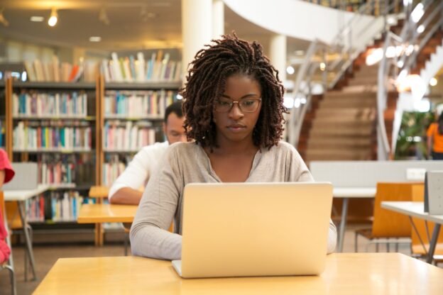 Étudiante africaine qui révise ses cours de droit en bibliothèque universitaire en Belgique